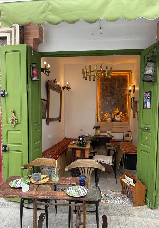 Notre devanture : volets verts ouverts sous un store vert, tables en terrasse