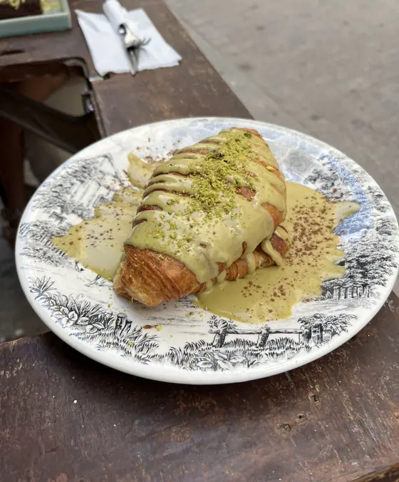 Croissant nappé d'une crème claire et de pistache concassée, sur une assiette à motif