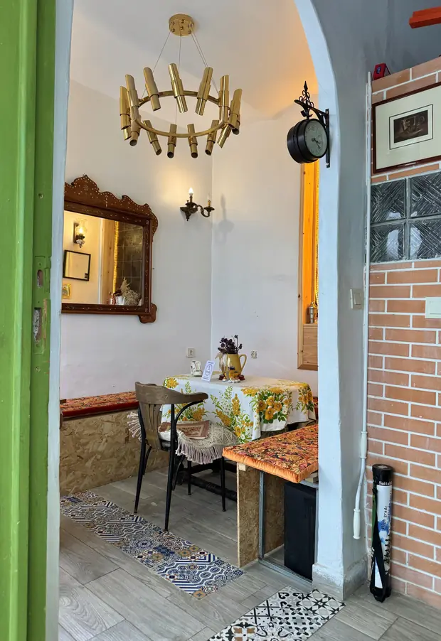 L'intérieur vu depuis la porte verte : lustre en laiton, miroir, banquette et table nappée
