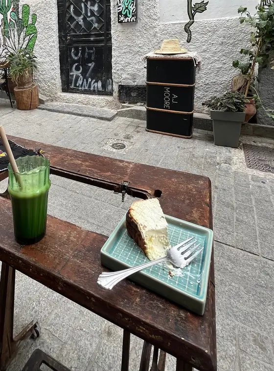 Un jus vert pressé et une part de gâteau blanc sur une table en terrasse, devant une fresque