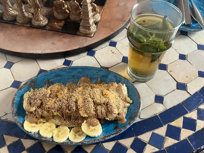 Un dessert à la banane sur une assiette turquoise, à côté d'un verre de thé à la menthe, sur une table en zellige